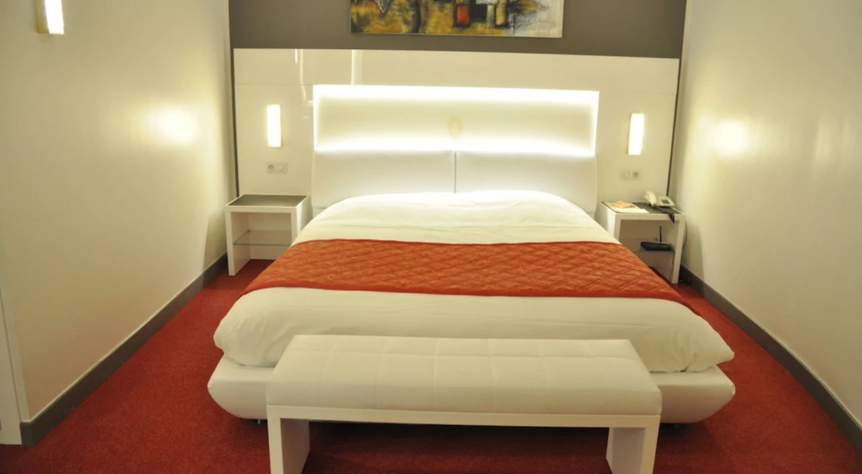 A hotel room with a large bed, a bedside table, a nightstand, and a painting on the wall.