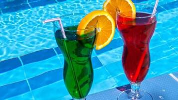 Two cocktails with straws and orange slices on a poolside table.