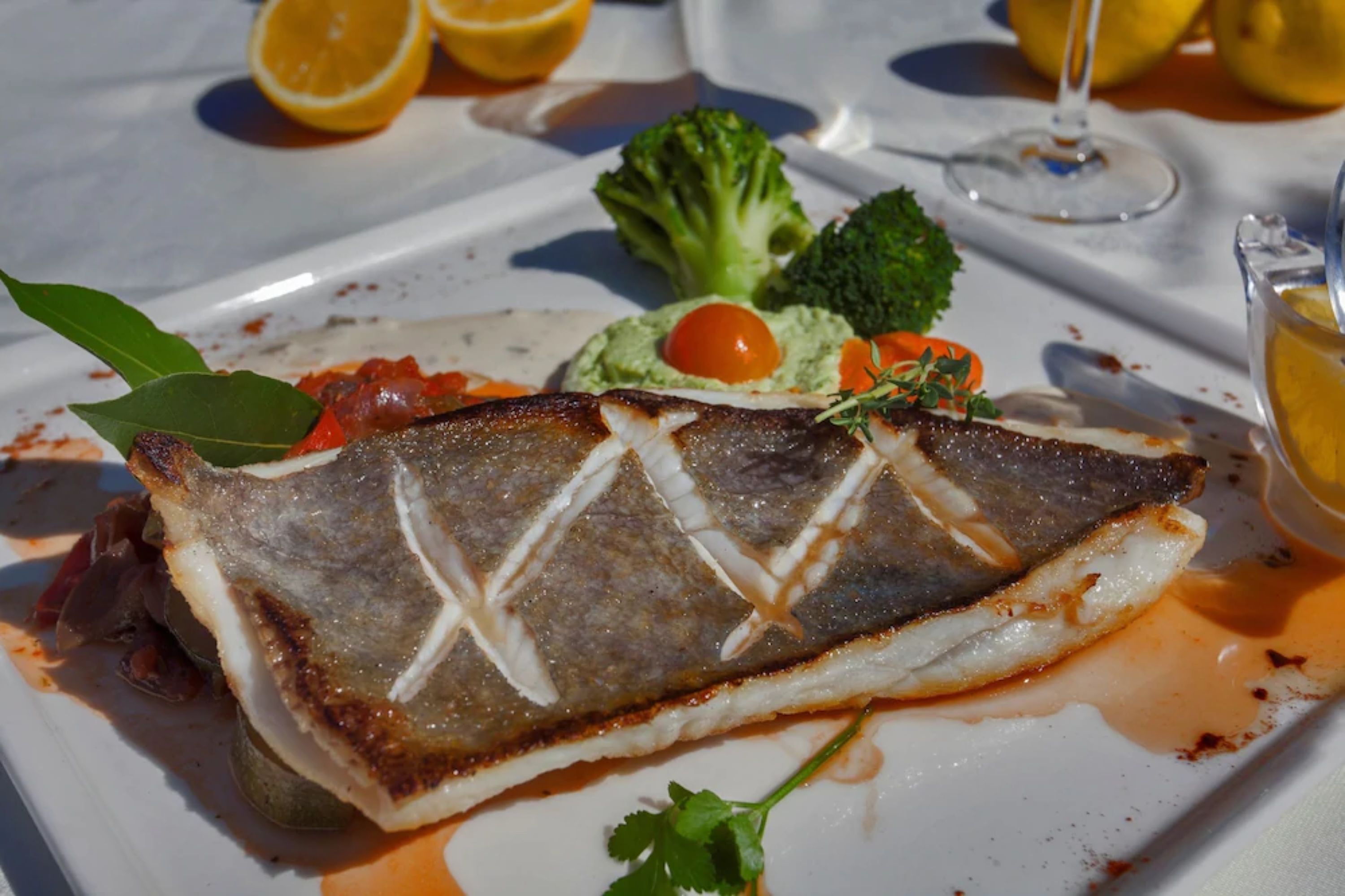A white plate with a grilled fish, vegetables, and a glass of white wine.