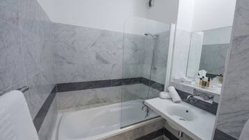 A modern bathroom with a glass-enclosed shower, a white sink, and a marble-tiled floor.