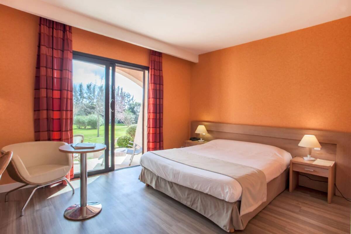 Habitación de hotel con cama, una silla, una mesita y una mesita de noche con lámpara.