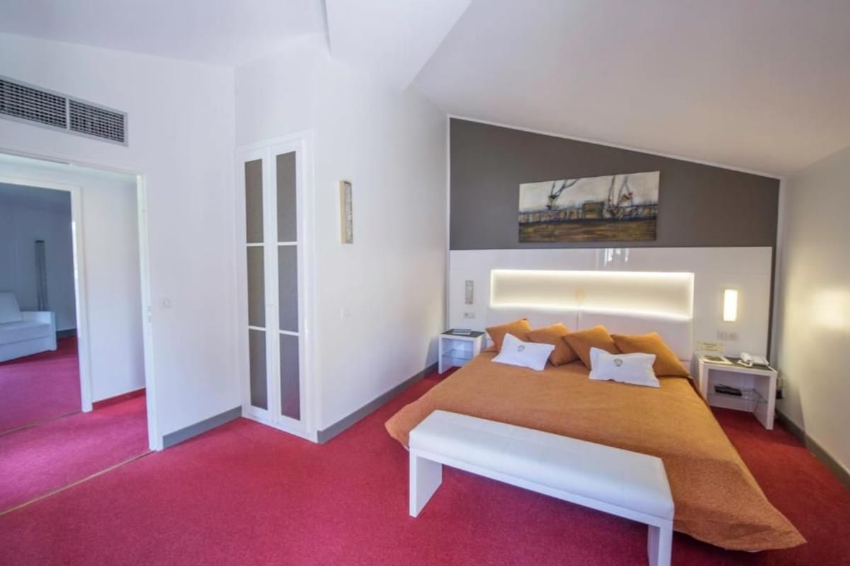 A modern hotel room with a large bed, a bench, a bedside table, and a nightstand.