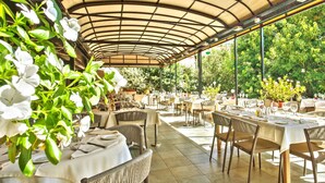 An outdoor dining area with tables and chairs, covered by a curved roof, surrounded by greenery. - Chez Walter (Lucciana)