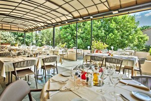 Un área de comedor al aire libre con mesas dispuestas para comidas, rodeada de árboles y una estructura de techo cubierto.