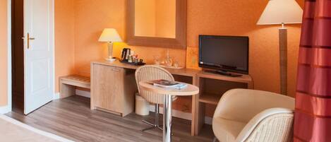 A hotel room with a bed, a desk with a computer, a chair, a small table, and a TV.