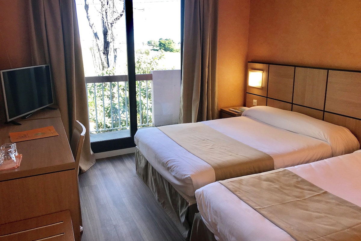A hotel room with a bed, a desk, a television, and a window with curtains.