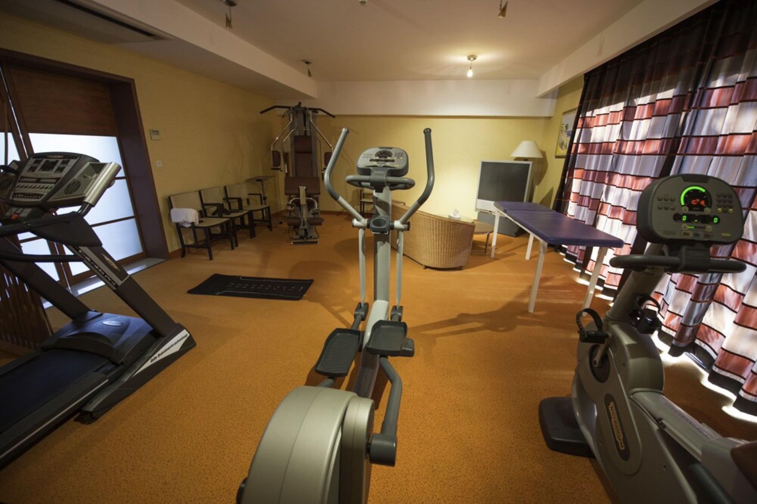 A gym with cardio machines, benches, and a television.