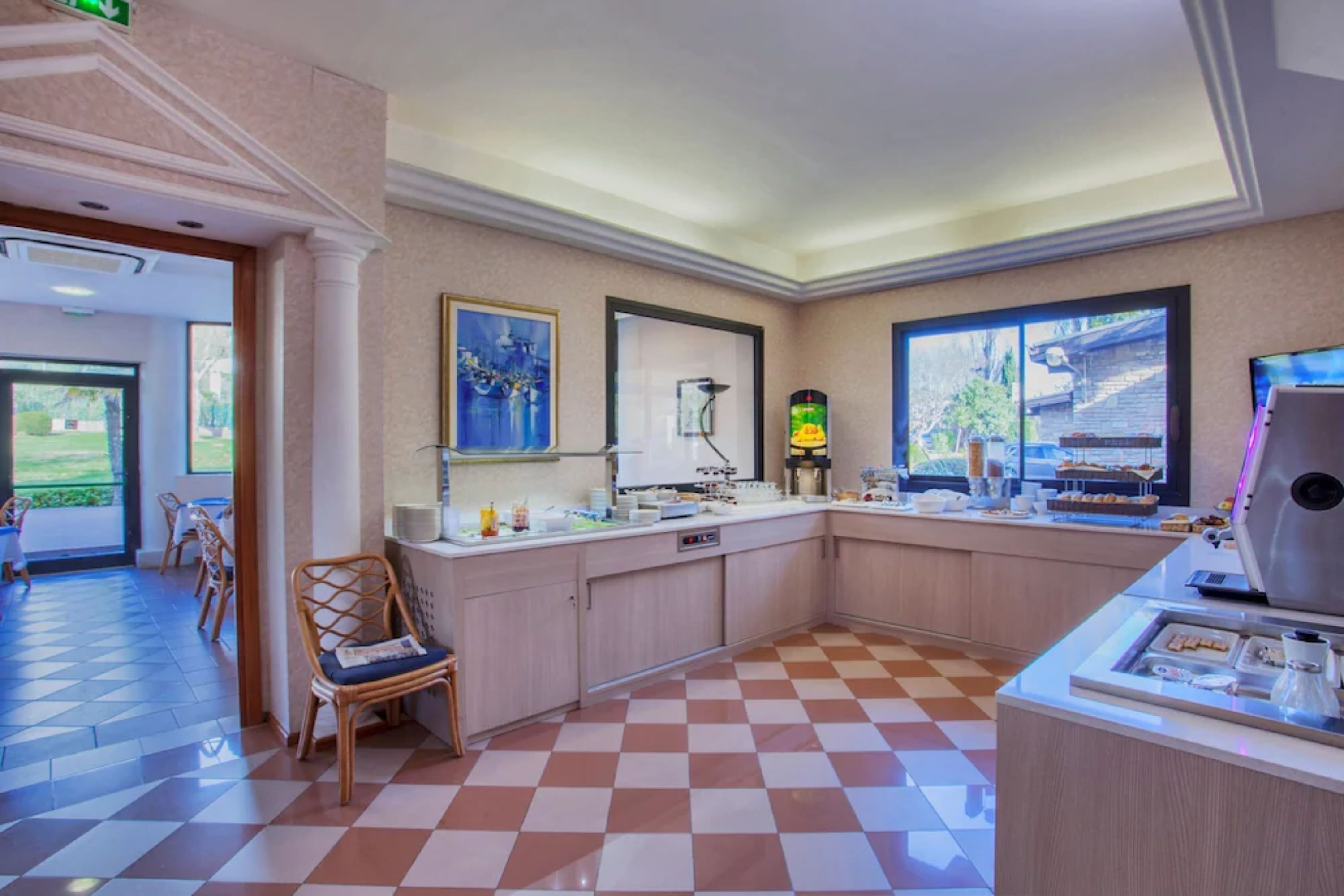 A hotel lobby with a checkered floor, a reception desk, a coffee machine, and a window with a view of greenery.