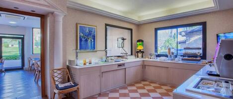 A hotel lobby with a checkered floor, a reception desk, a coffee machine, and a window with a view of greenery.