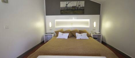 Une chambre d’hôtel moderne avec un grand lit, une tête de lit dotée d’un éclairage intégré, un tableau au mur et des tables de chevet avec des lampes.
