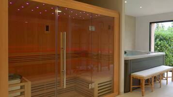 A modern bathroom with a glass-enclosed shower, wooden bench, and a view of greenery outside.