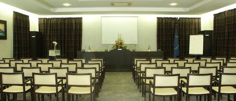 A conference room with rows of chairs, a podium, a projector screen, and curtains.