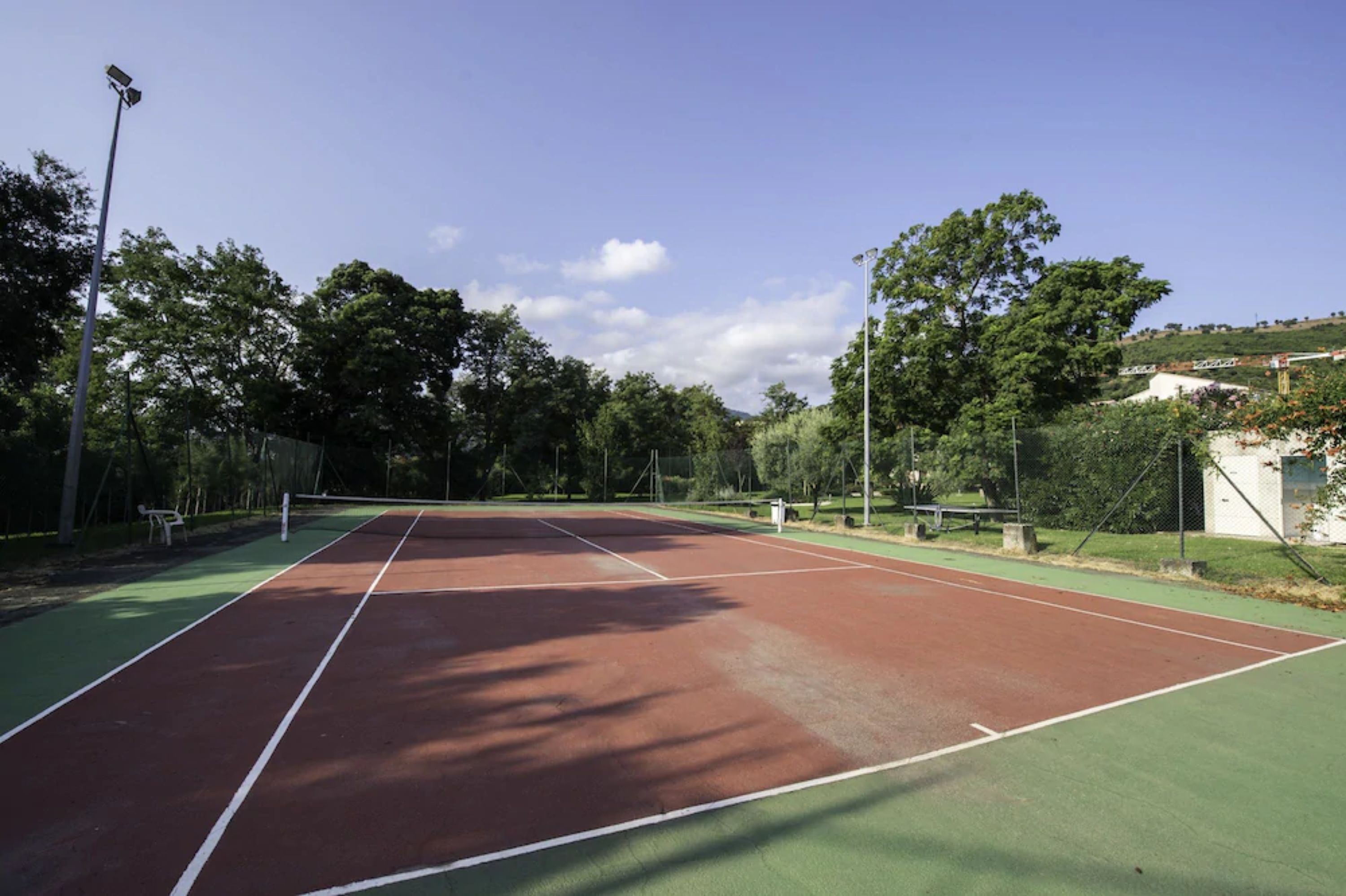 A tennis court with a net, surrounded by trees and a fence.