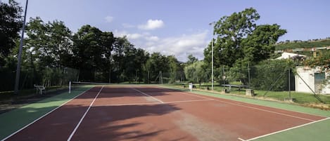 A tennis court with a net, surrounded by trees and a fence.