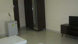 A room with a white desk, a small refrigerator, a dark wooden cabinet, and a television on a stand.