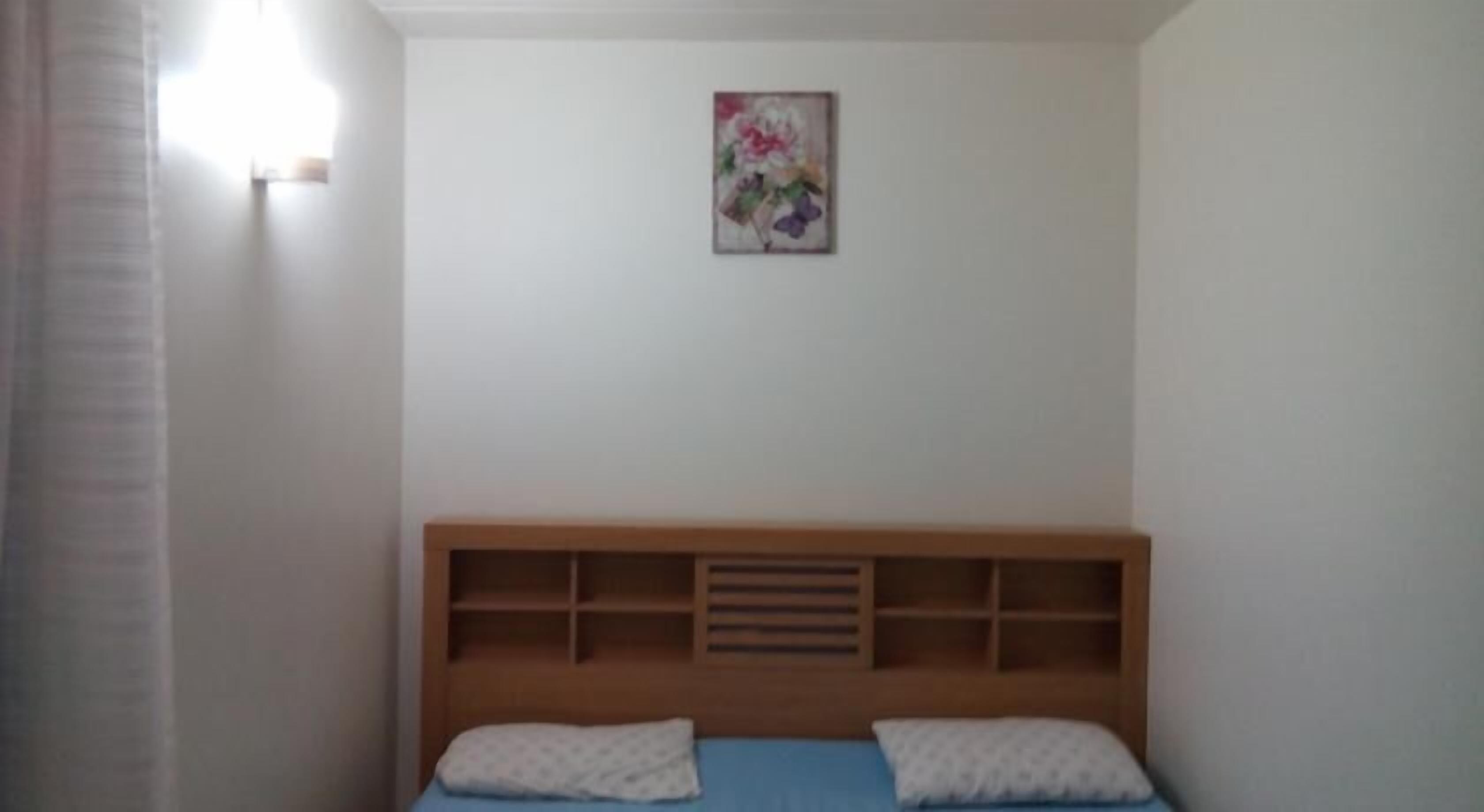 A bedroom with a wooden headboard, two pillows, and a floral artwork on the wall.