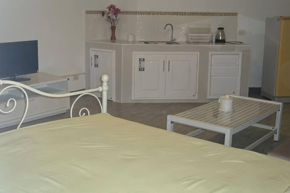 A bed, a small table, a TV, a kitchen area with cabinets, a sink, and a refrigerator.