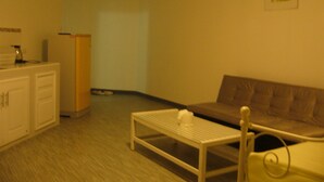 A small, sparsely furnished room with a white table, a brown sofa, a cabinet, and a refrigerator.