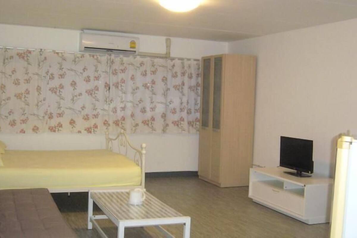 A small, simple room with a bed, a TV, a small table, and a sofa.