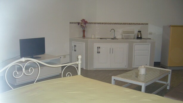 A room with a bed, a small table, a TV, a kitchenette with cabinets, and a refrigerator.