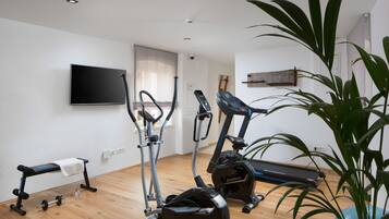 Une salle de sport à domicile équipée d’appareils d’exercice, d’un banc et d’un téléviseur fixé au mur.
