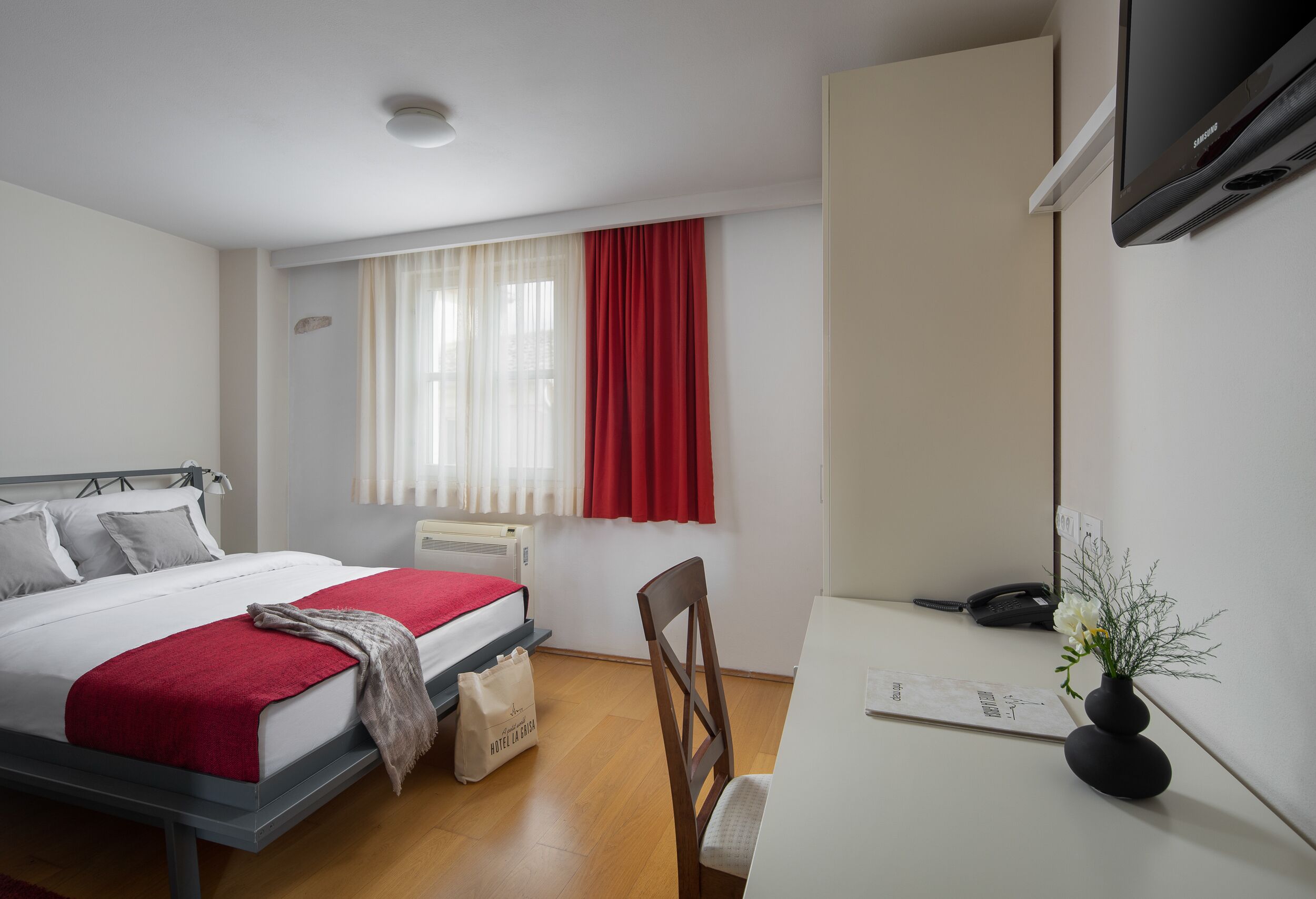 Une chambre d’hôtel avec un lit, un bureau, une chaise, une télévision et une fenêtre avec des rideaux.