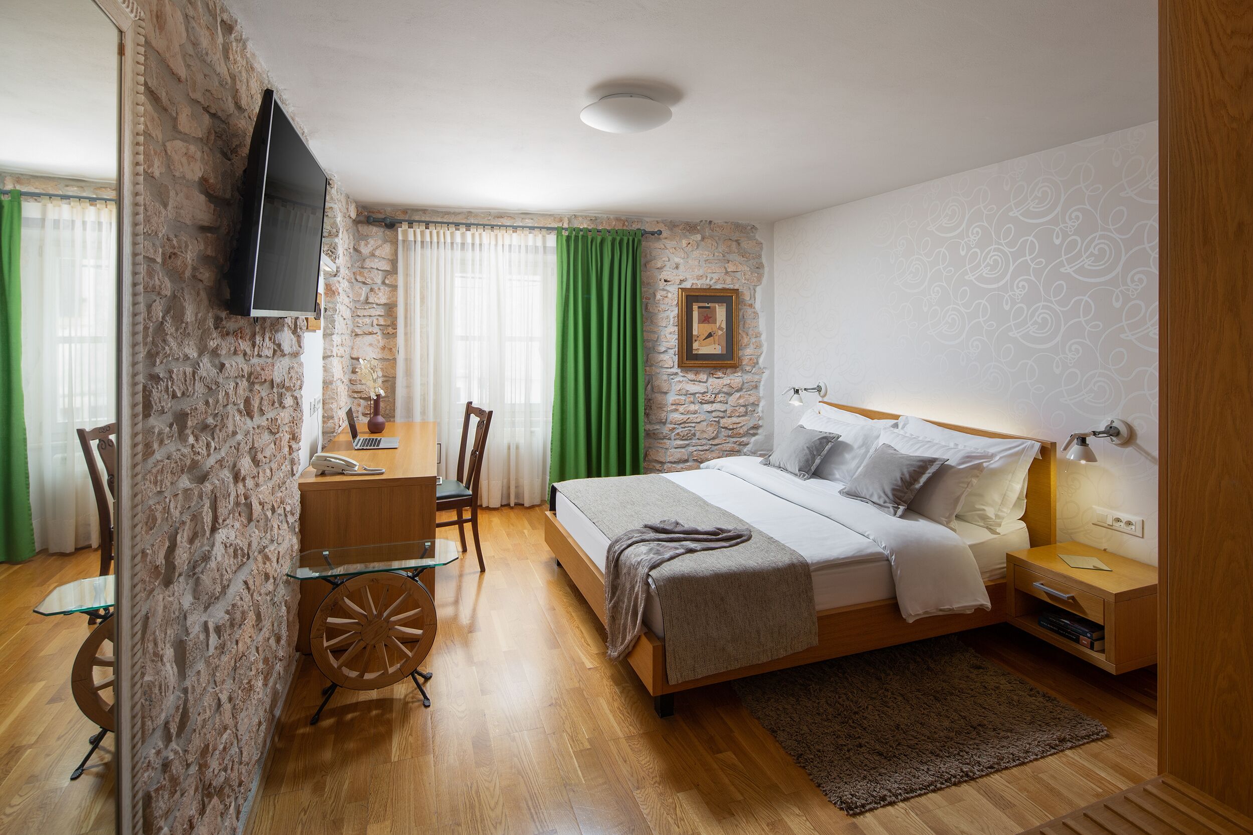 A bedroom with a bed, bedside table, lamp, and a desk with a chair.