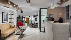 A modern hotel lobby with a reception desk, a sofa, a red chair, and a dining area with tables and chairs. - Hotel La Grisa (Bale)