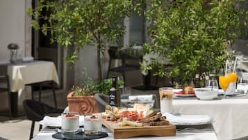 Une table dressée pour le petit-déjeuner, avec une variété d’aliments, notamment du fromage, du pain et une boisson, le tout posé sur une nappe blanche.
