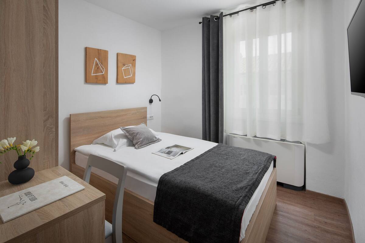 A modern hotel room with a wooden bed, white bedding, a bedside table with a vase of flowers, and two wall art pieces.