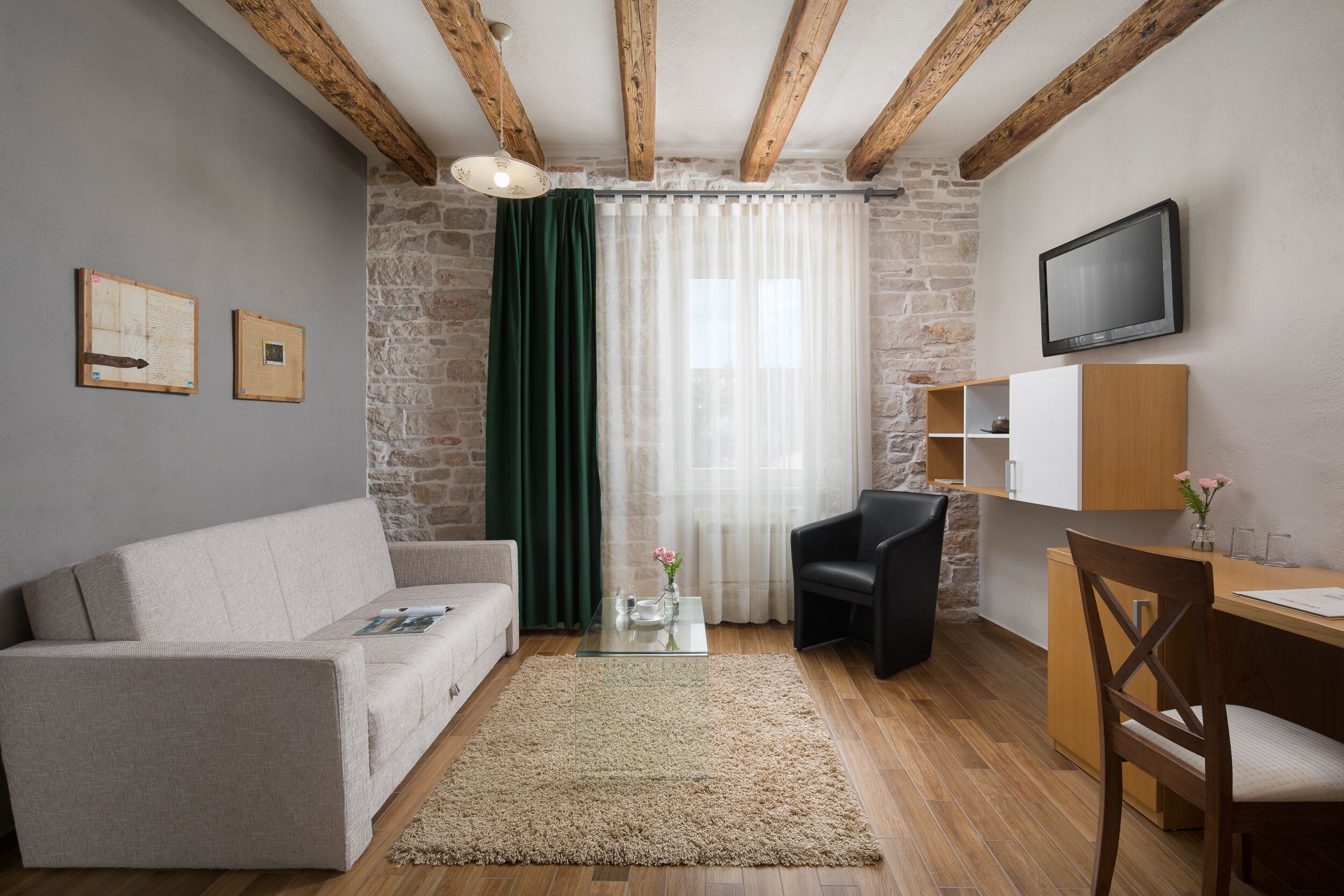 Un salon chaleureux avec un canapé, une table basse, un téléviseur fixé au mur et un mur en pierre.