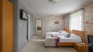 A bedroom with two beds, a wooden wardrobe, a stone wall, and a mirror.