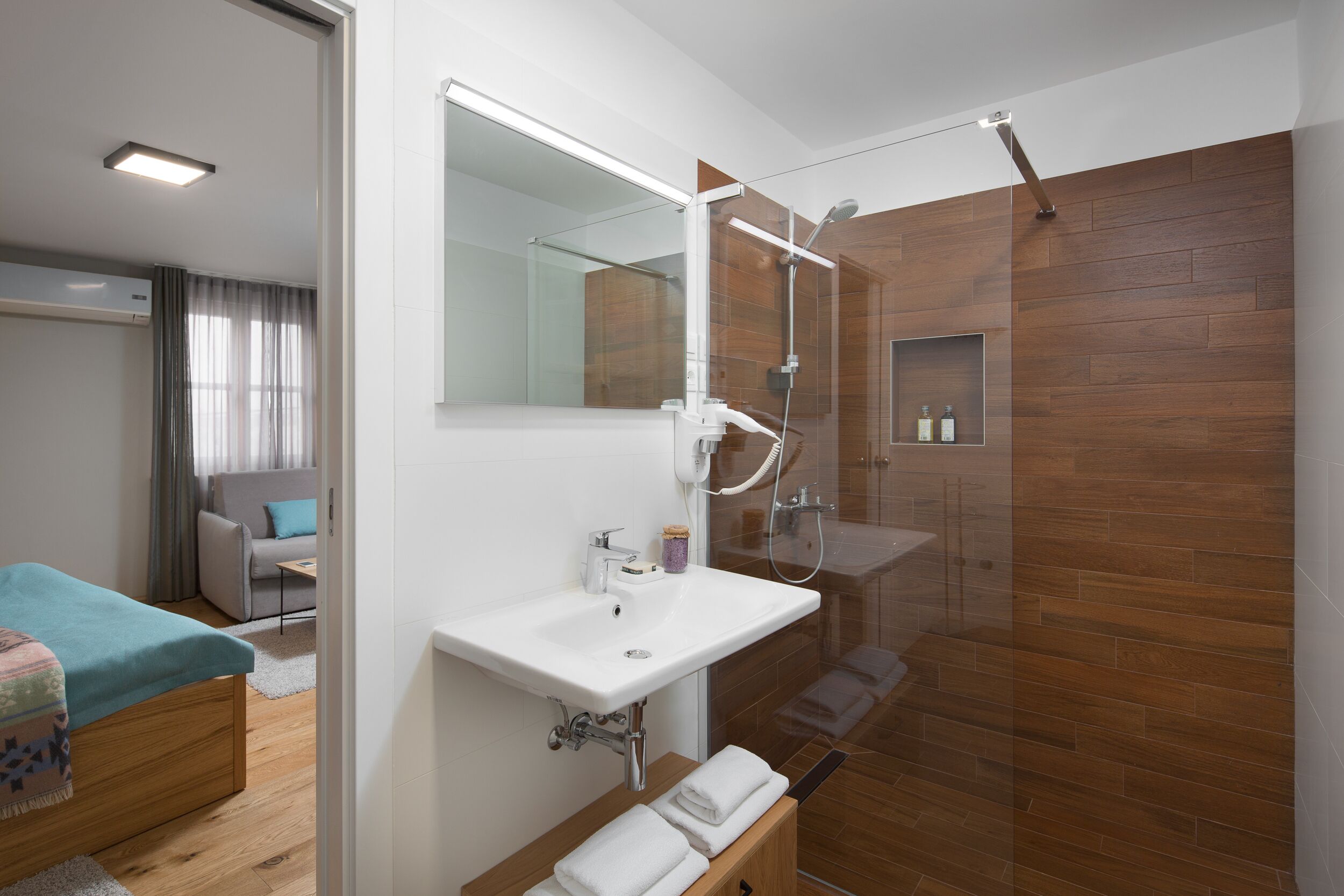 Un baño moderno con cabina de ducha de vidrio, lavabo blanco y tocador de madera.
