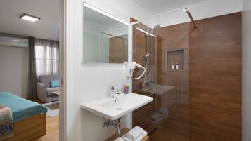 Un baño moderno con cabina de ducha de vidrio, lavabo blanco y tocador de madera.