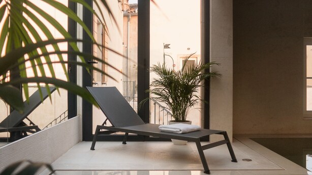 A modern indoor pool with clear glass walls, lounge chairs, and potted plants. - Hotel La Grisa (Bale)