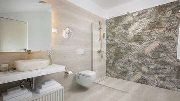 A modern bathroom with a large mirror, a sink, a toilet, and a shower area with a leaf-patterned wall.