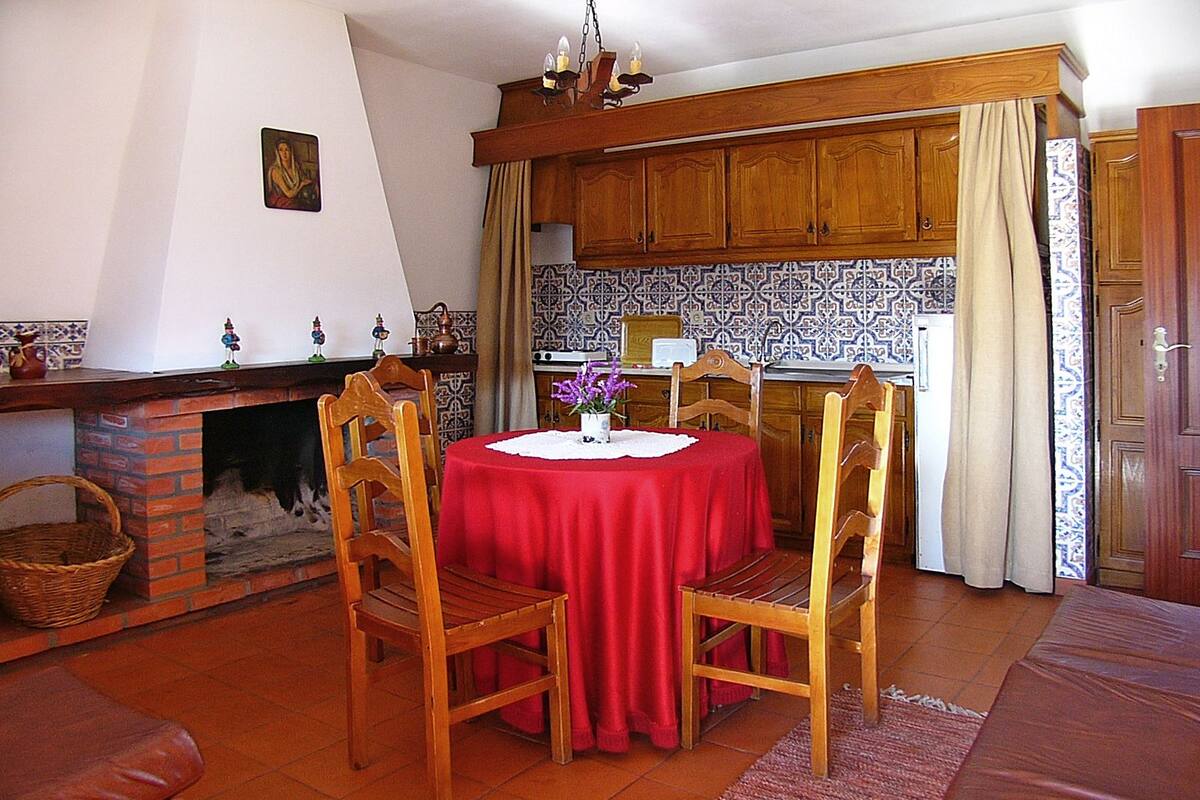 Uma sala de jantar com toalha de mesa vermelha, cadeiras de madeira, lareira e ladrilhos estampados.