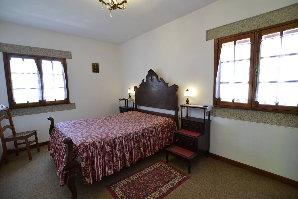 Quarto com cama, cadeira, mesa de cabeceira, cômoda e janela.