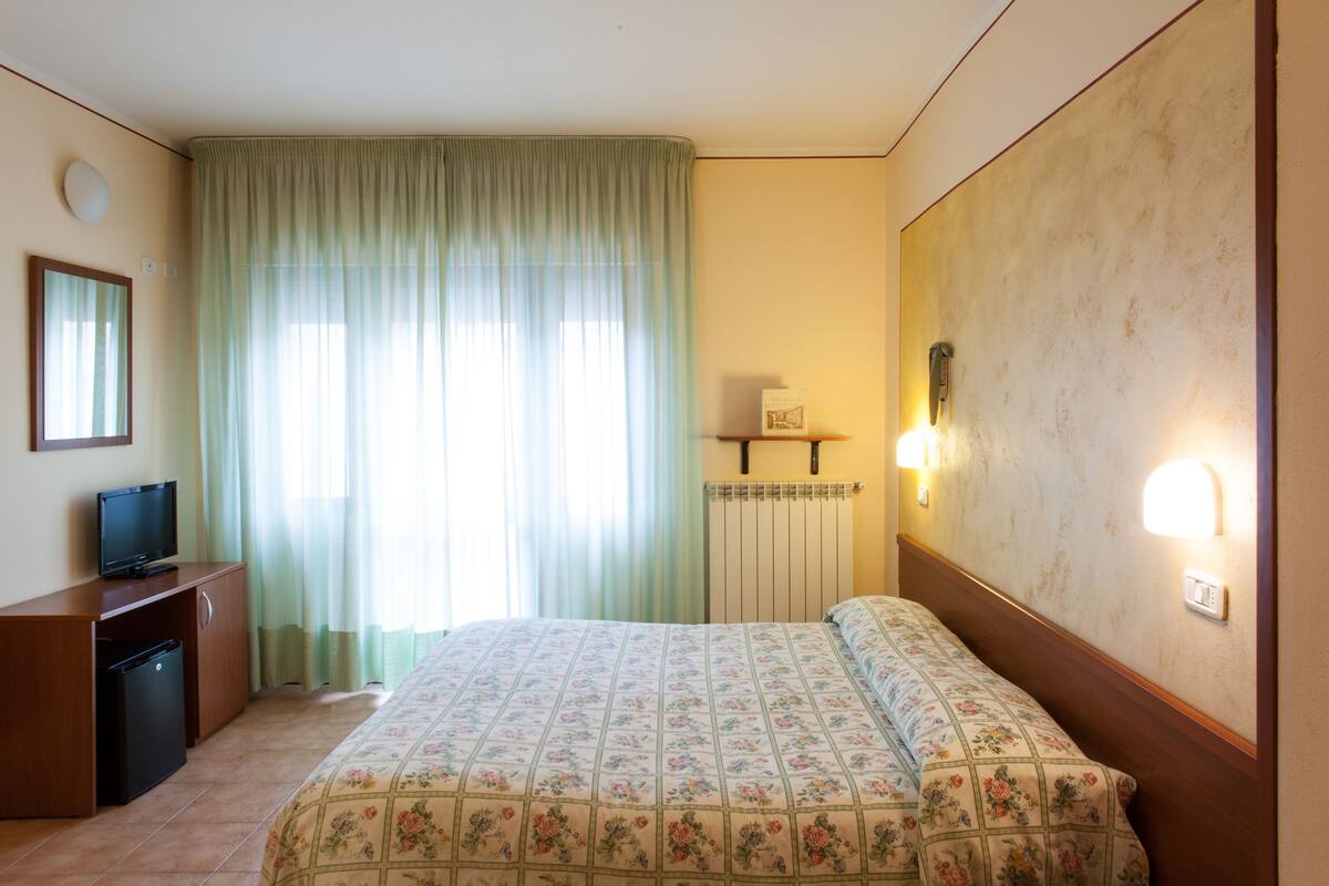 Une chambre d’hôtel comprenant un lit, un bureau avec une télévision, un radiateur et un luminaire fixé au mur.