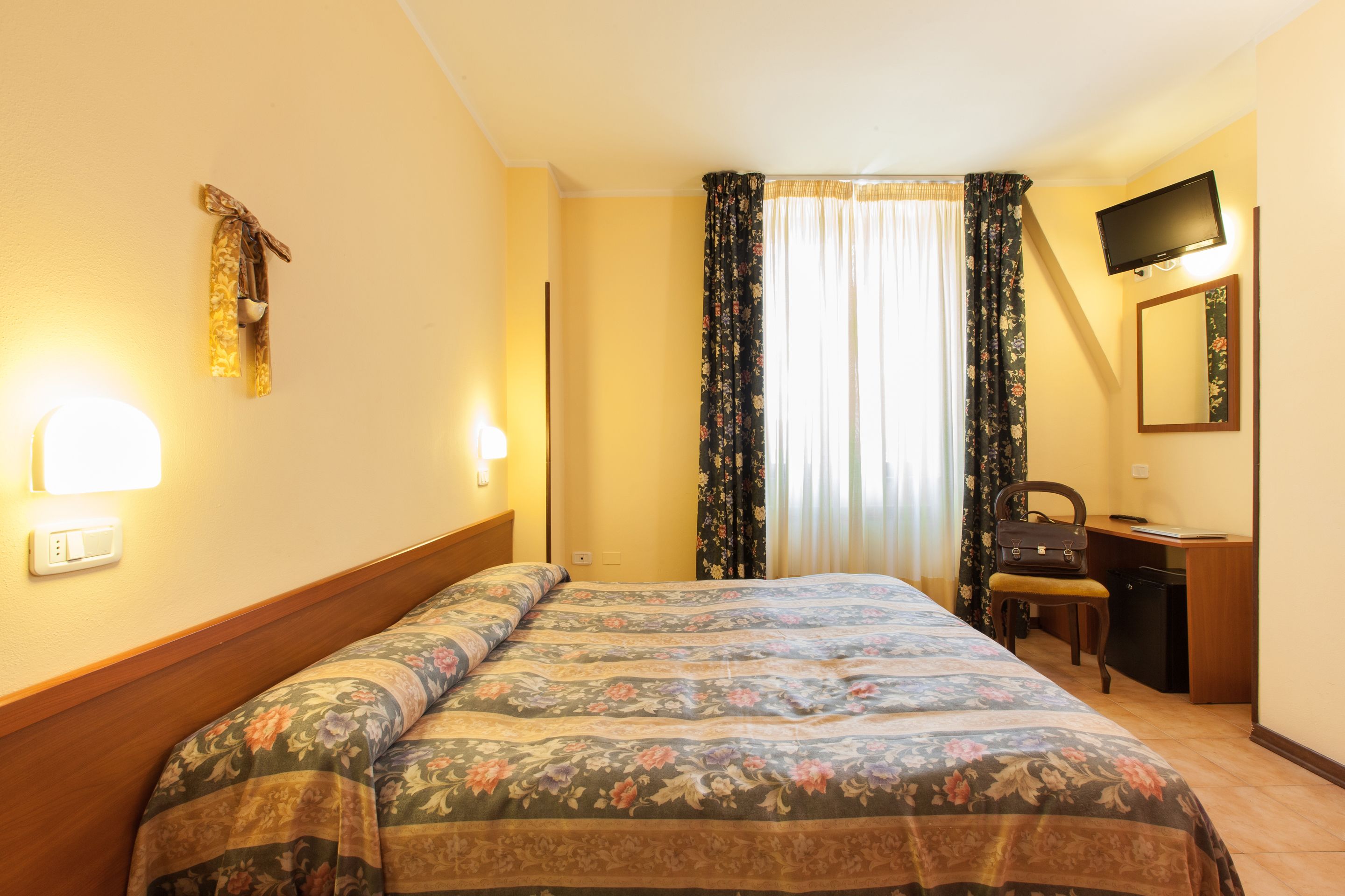 A hotel room with a bed, a desk, a chair, a television, and curtains.