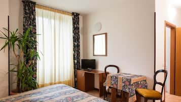 Una camera da letto con due letti, una scrivania, una sedia, una televisione e una pianta in vaso.