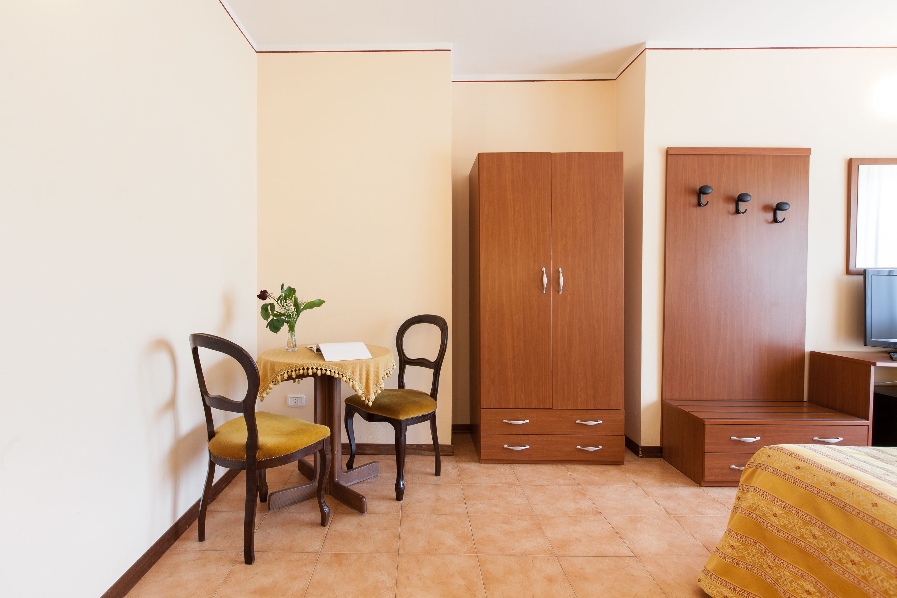 Ein Schlafzimmer mit Bett, einem Holzschrank, einem Schreibtisch mit Stuhl und einem kleinen Tisch mit Pflanze.