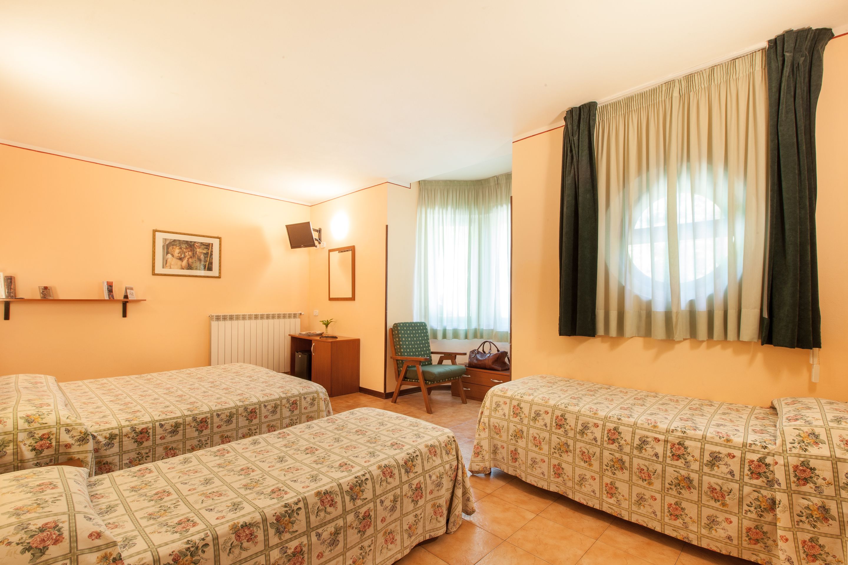Une chambre d’hôtel avec deux lits simples, un bureau, une chaise, un radiateur et une fenêtre avec des rideaux.