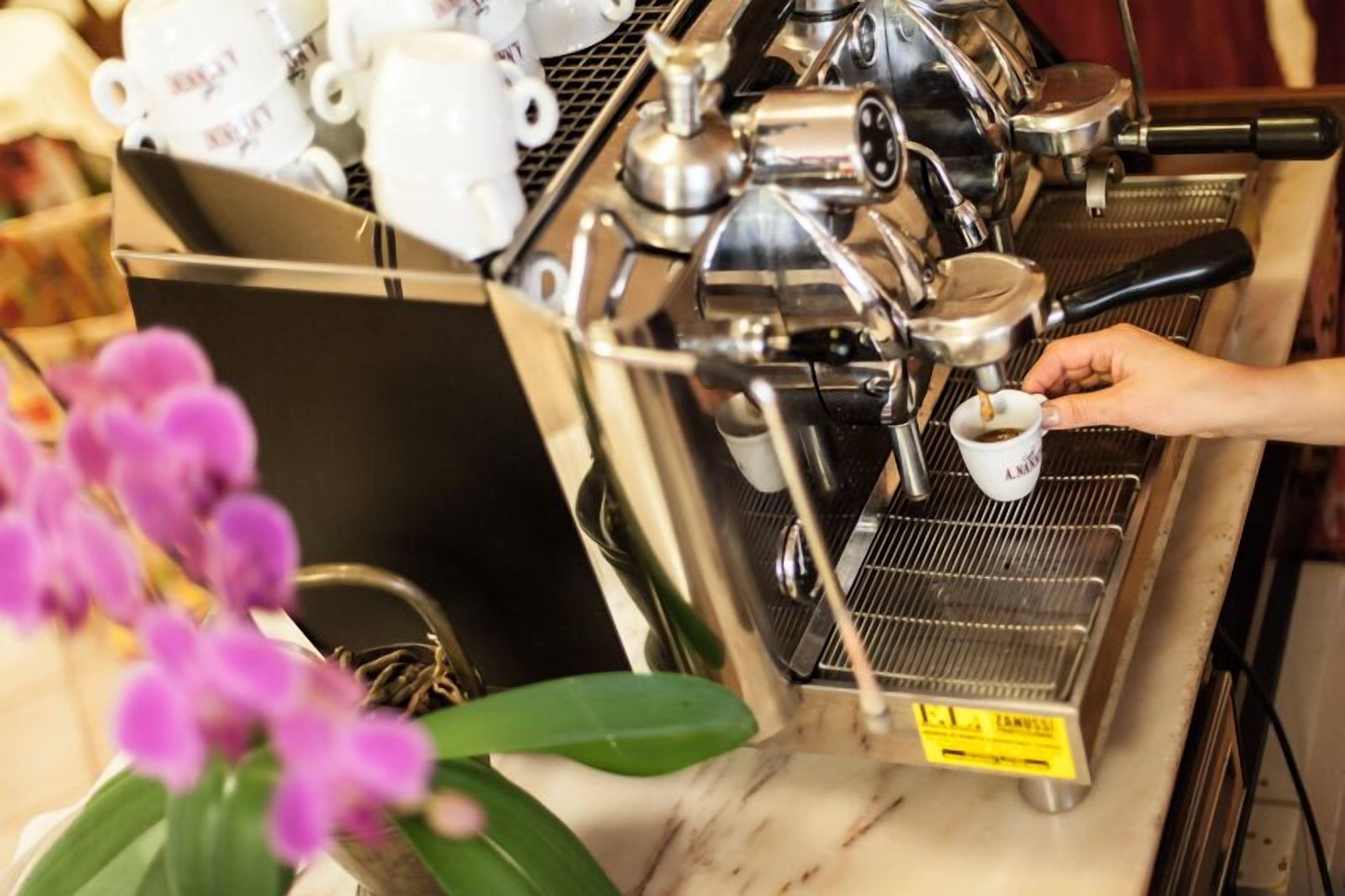 A coffee machine with a hand holding a cup, and a tray of white cups in the background.