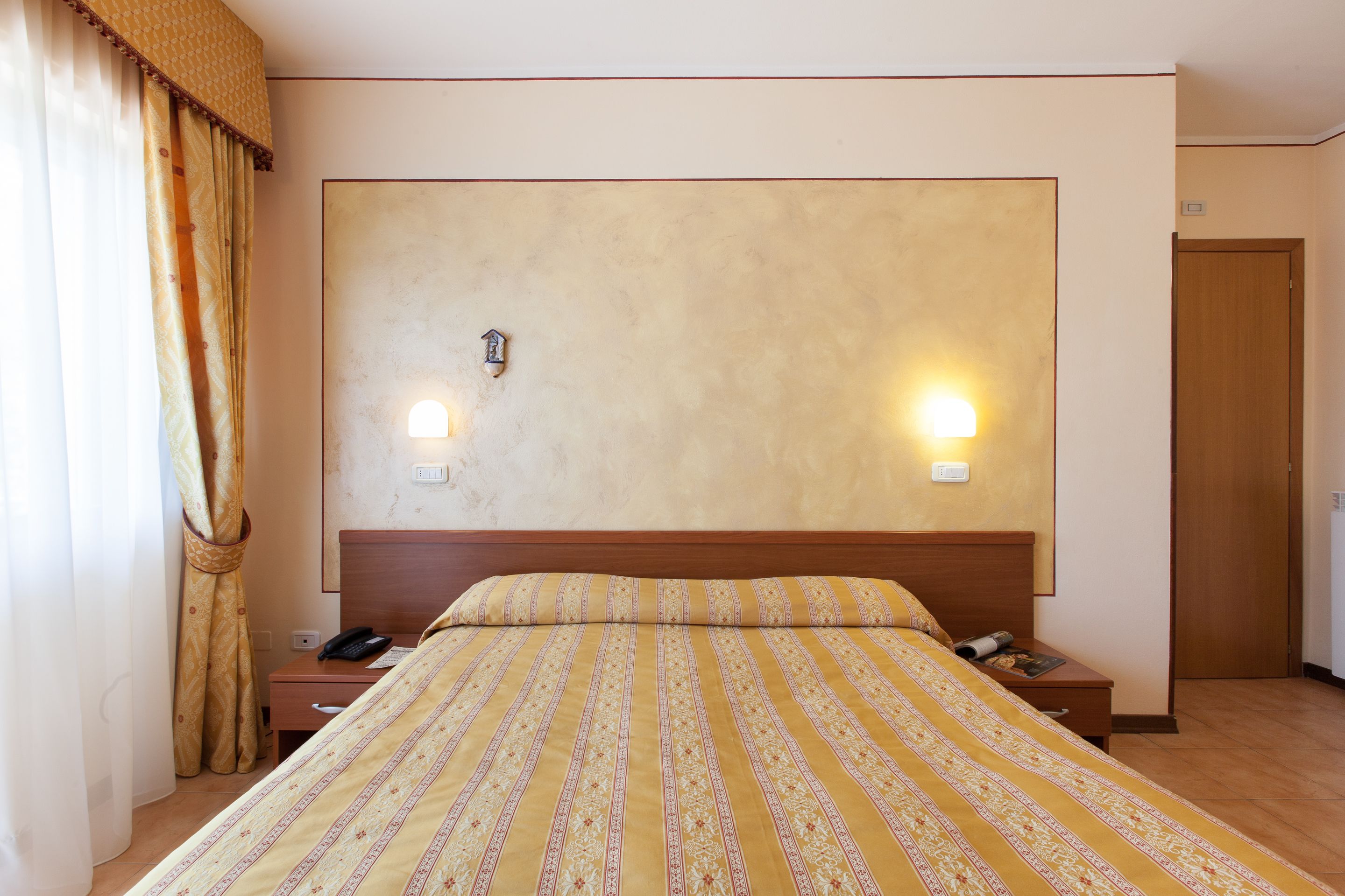 A hotel room with a large bed, two bedside tables, a nightstand, a wooden headboard, and a door.