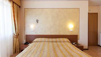 A hotel room with a large bed, two bedside tables, a nightstand, a wooden headboard, and a door.