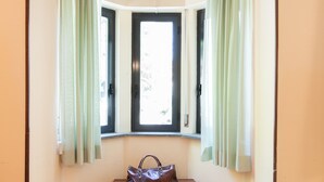 A room with a bay window, a wooden bench, and a brown handbag on the bench.