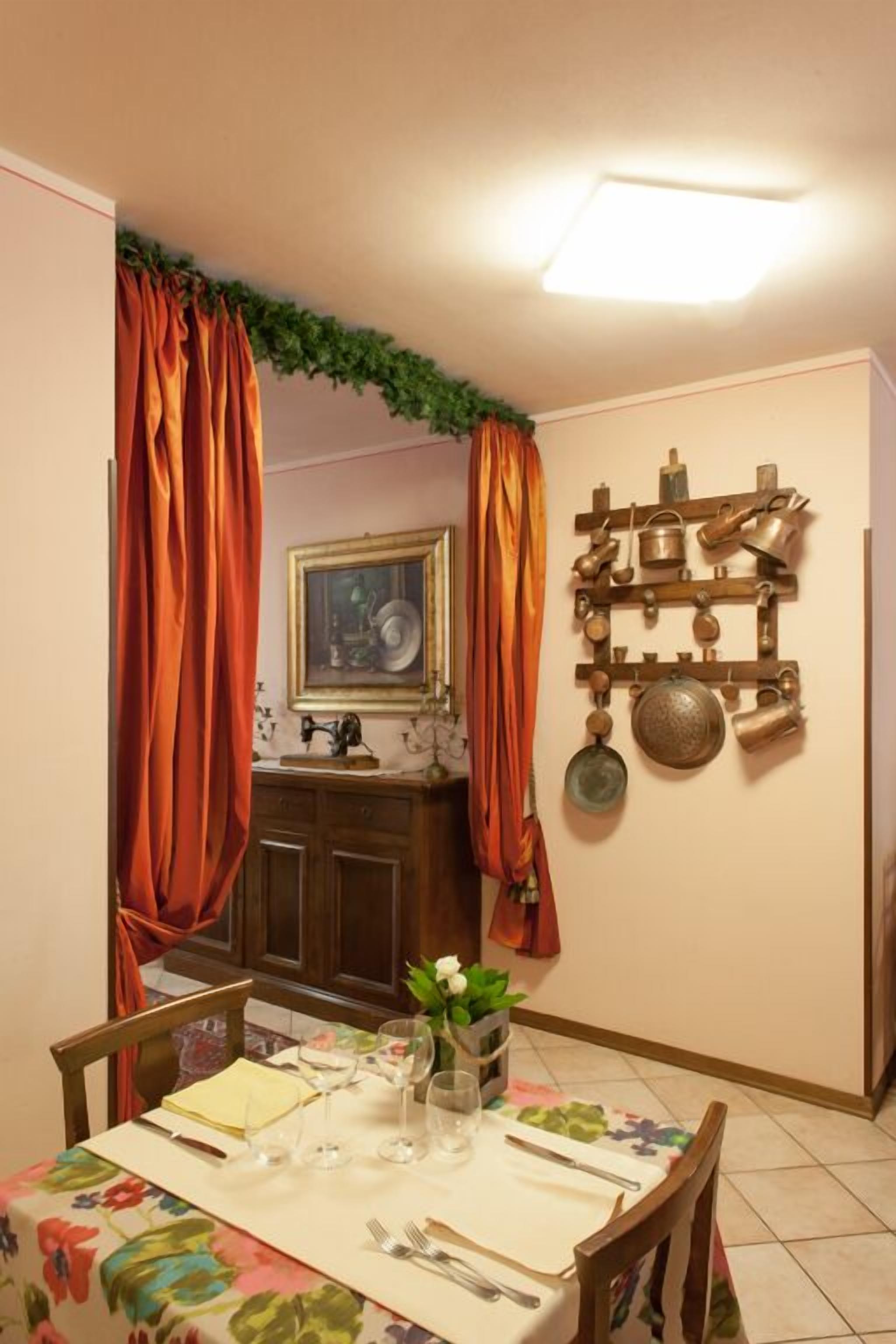 A dining area with a table set for two, a wall-mounted pot rack, and a painting above the sink.