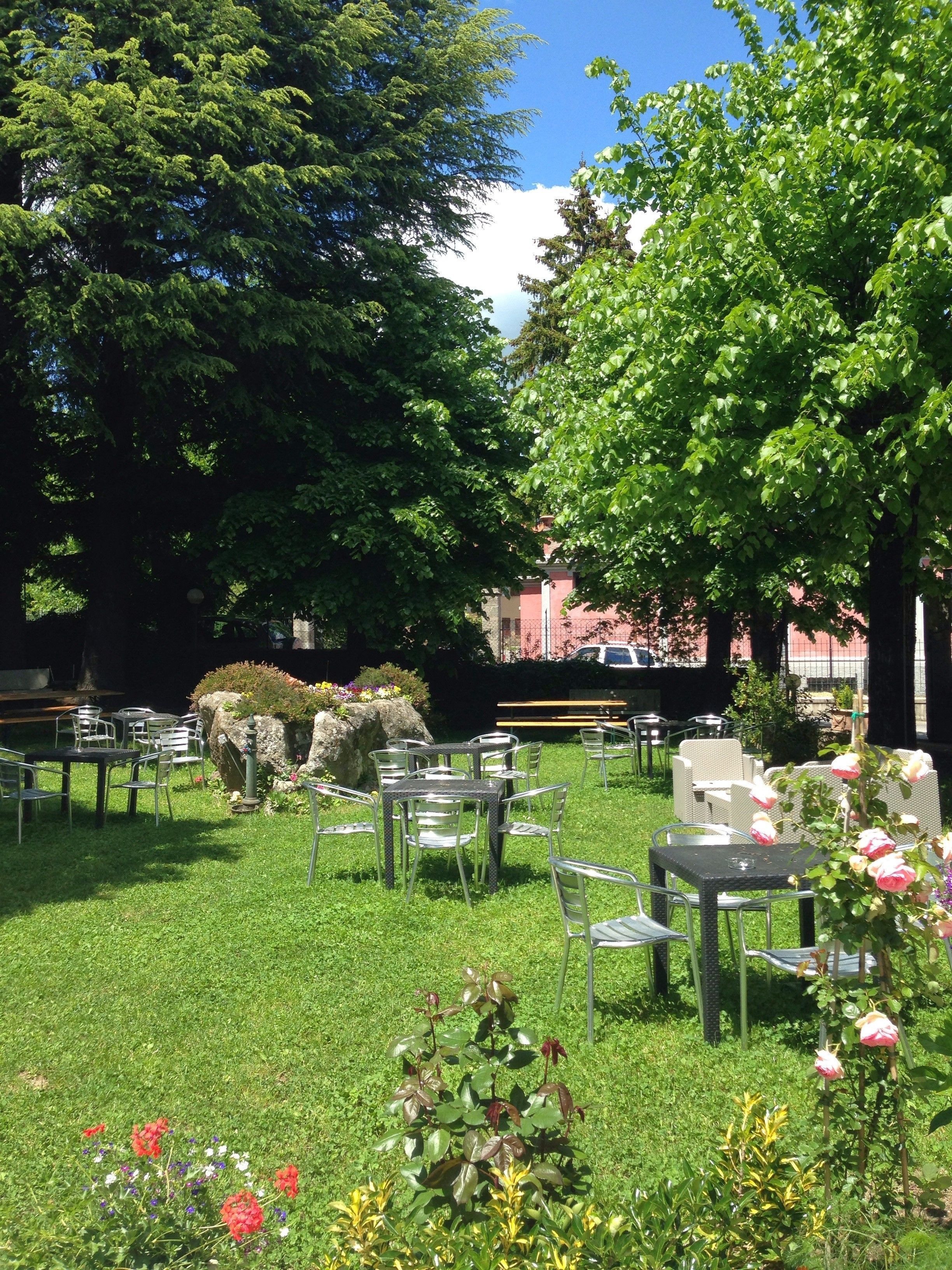 Un'area salotto all'aperto con tavoli e sedie, circondata da vegetazione e fiori.