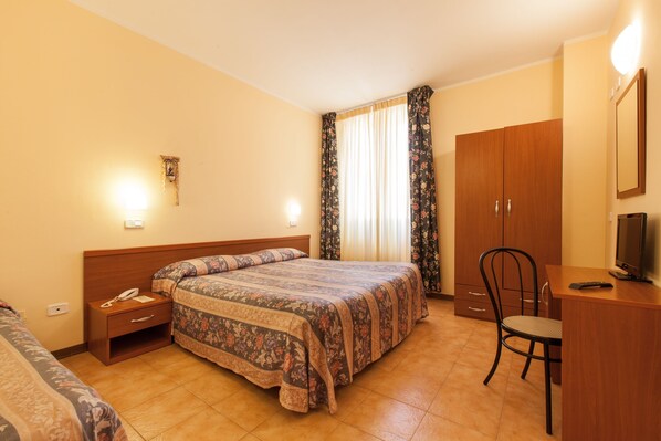 Una habitación de hotel con una cama, un escritorio con silla, un armario y un televisor.